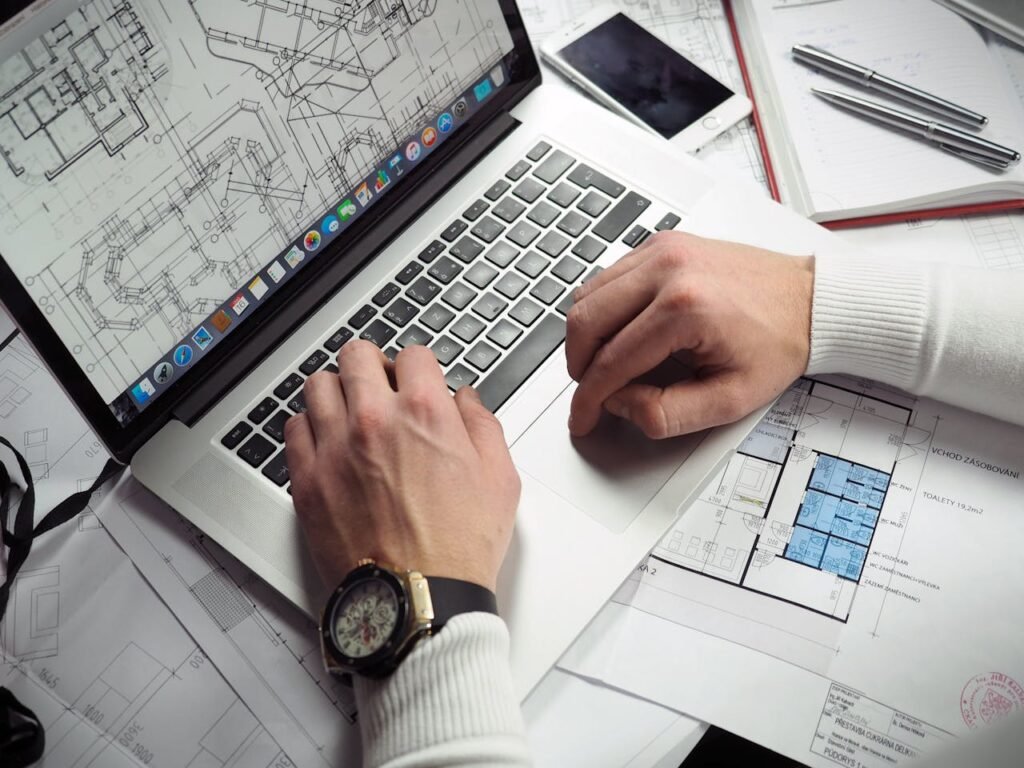 pexels-photo-110469 Architect reviewing detailed floor plans and schematics on a laptop with a smartphone nearby.