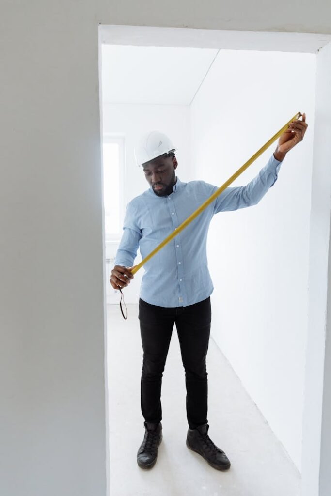 pexels-photo-8470780 Adult male construction worker measuring room dimensions with a tape measure.